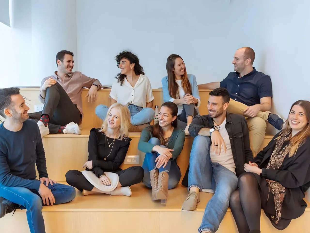 A smiling group of monday experts sitting together on wooden steps